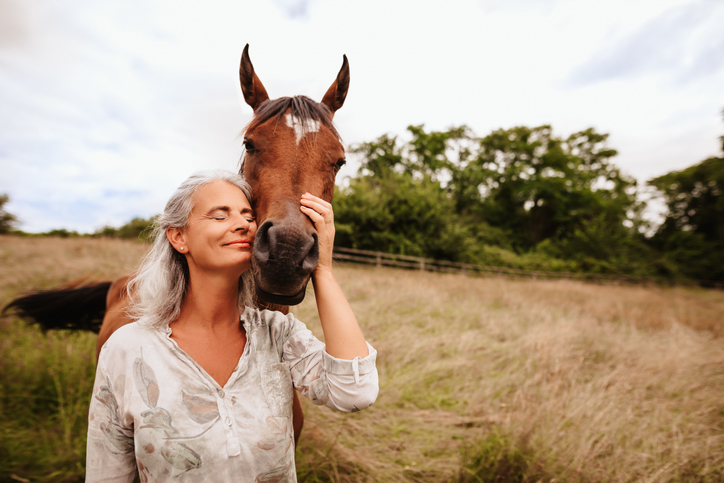 Beautiful mature woman enjoying with closed eyes her brown arabian mare in the free nature